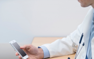Doctor sitting at desk looking at cell phone.
