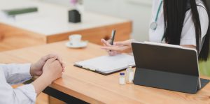 Doctor and patient sitting at desk. Doctor taking notes with computer on desk.