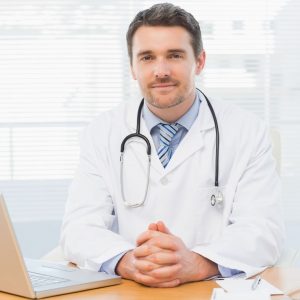 Doctor sitting at desk in front of laptop.